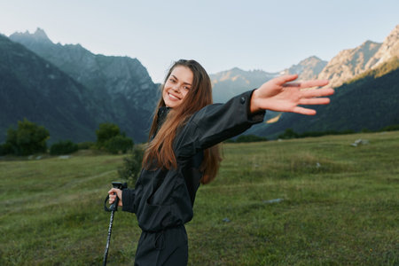 A cheerful hiker stands with arms outstretched in a scenic valley beneath rugged mountains. Bright daylight and an expansive sky create a sense of freedom, adventure, and positive energy in thisの写真素材