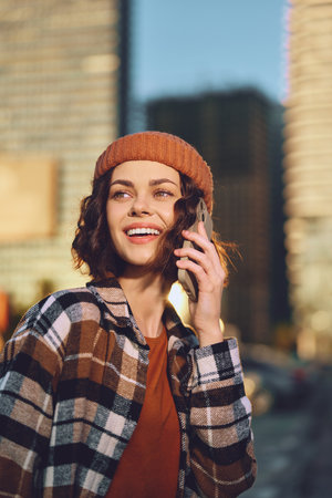woman phone smile urban beanie plaid candid golden authenticity, candid lifestyle and golden hour glow capture mindful living and emotional storytelling in a warm city portrait.の写真素材