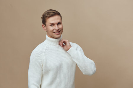 Smiling man wearing white knitted sweater looking at camera relaxed cheerful casual portrait isolated on plain beige background studio shot. People lifestyle conceptの写真素材
