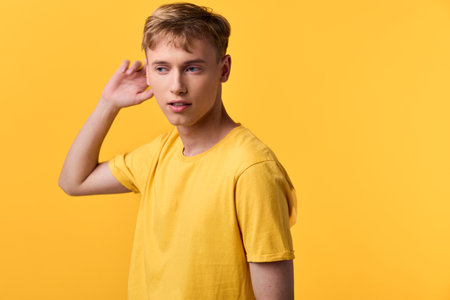 Young man in a bright yellow shirt against a vivid yellow backdrop, posing with a thoughtful glance, casual studio setup, emphasizing color harmony and relaxed style for lifestyle and fashion themesの写真素材
