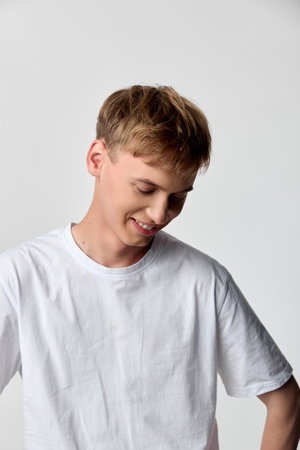 Smiling boy in white tshirt relaxes in a studio setting, casual mood and simple pose, soft lighting highlighting youth and cheerful expressionの写真素材