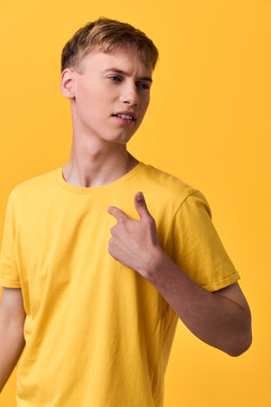 Young male in a yellow tshirt against a bright yellow background pointing at himself casual lifestyle shot with bold color and confident expression studio lighting minimal setupの写真素材