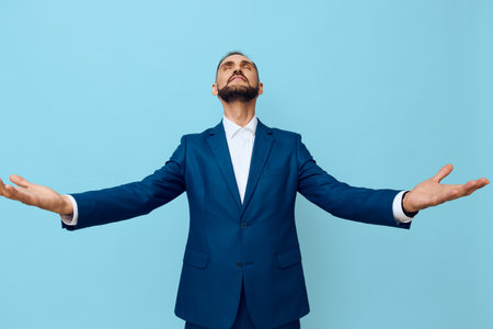 A confident business professional stands alone against a solid blue background, arms open wide, exuding triumph and gratitude in a calm, focused mood.の写真素材
