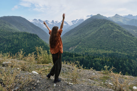 woman mountains hiking nature outdoors landscape on ridge arms raised at summit, authentic inclusive solo traveler enjoying wilderness freedom scenic viewの写真素材