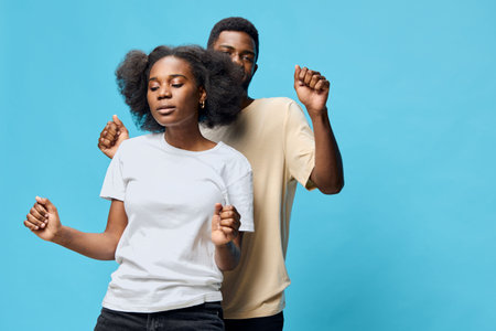 A joyful couple dancing together against a soft blue background, showcasing playful emotions and contemporary casual fashion in a vibrant settingの写真素材