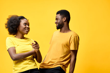 Happy young African couple sharing a joyful moment in matching yellow outfits against a bright yellow background, exuding positivity and connectionの写真素材
