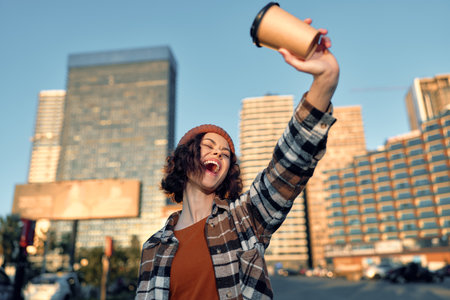 woman with coffee cup, joy and candid lifestyle in city street at golden sunlight, beanie and plaid jacket, authenticity and emotional storytelling of mindful living momentの写真素材