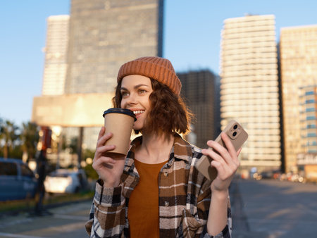 woman with coffee and smartphone on urban street, smiling in candid shot with authenticity and golden hour glow. Mindful living and emotional storytelling of modern city life.の写真素材