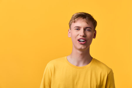 Young man wearing a yellow shirt stands against a vivid yellow background, creating a bright,...
