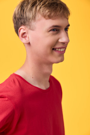 Smiling young man in a red shirt shown in profile against a bright yellow backdrop, conveying...