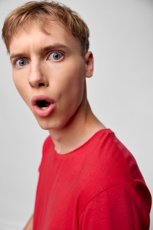 Surprised man in a red shirt with wide eyes and open mouth, closeup expression conveying shock and...