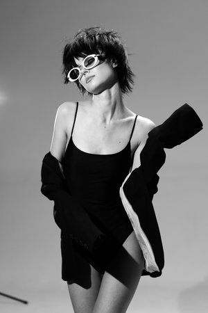 Black and white portrait of a stylish woman wearing sunglasses and a dark outfit with confident pose.の写真素材