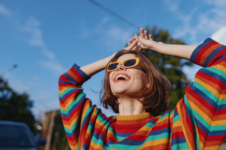 Woman smile sunglasses rainbow sweater joyful outdoor portrait happiness captured in sunlight, young woman in colorful casual fashion expressing carefree energy and radiant cheerful expression.の写真素材