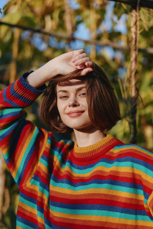 Young woman in her early 20s wearing a colorful striped sweater, smiling portrait outdoor in golden...
