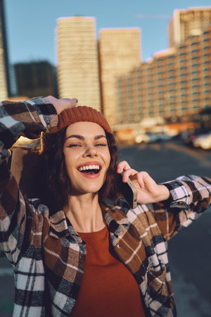 woman smile phone city beanie jacket sunlight candid portrait of a joyful woman on phone in urban golden hour glow, authenticity, mindful living and emotional storytellingの写真素材