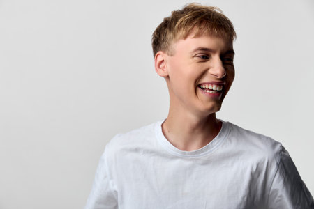 Smiling man in a white shirt exudes casual happiness, a bright expression captured in a clean studio...
