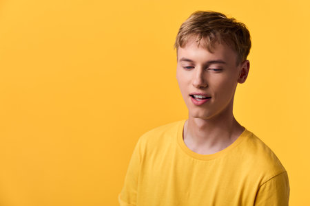 Young man in a yellow tshirt against a matching yellow studio background, relaxed pose and soft expression, vibrant color mood for fashion or lifestyle useの写真素材