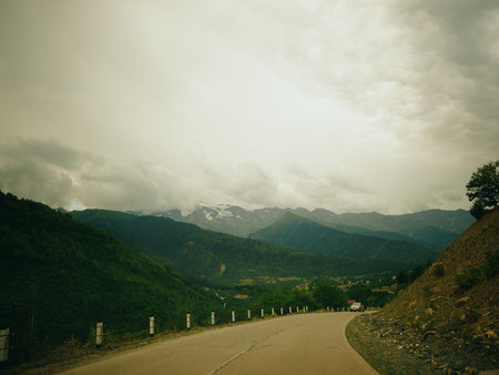 Winding road through rugged mountains offers a sweeping landscape under a muted, cloudy sky, with...
