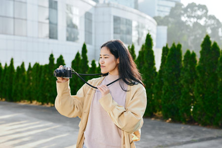 Camera in hand, woman photographs outdoors in an urban setting with a casual jacket, focused...