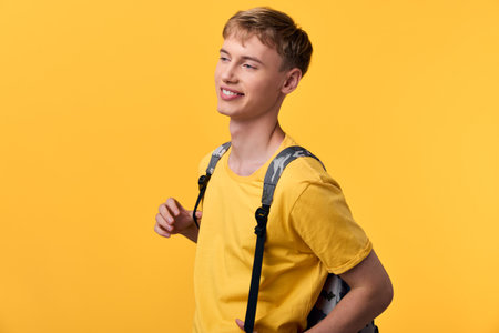 Smiling youth in a bright yellow t shirt with a backpack against a vibrant backdrop, conveying...