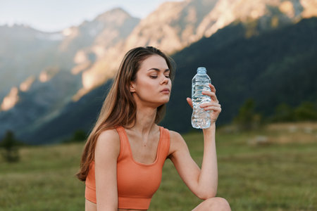 A focused young woman sits outdoors in a scenic valley, wearing an orange athletic top and holding a...