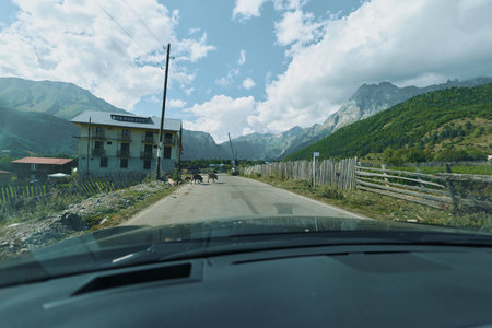 A scenic rural road winds through a mountainous valley, viewed from inside a car. Clear blue sky,...