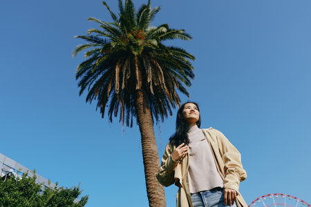 Palm, outdoor, woman, casual, sunny, sky, park, breeze, leisure, travel, scenery, sunlight, nature, summer, urban, street, pose, fashion, denim, cardigan, sneakers, confidence, expression, horizon,の写真素材