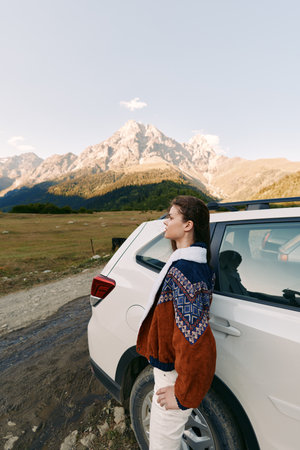 Woman standing by white car on a dirt road with towering mountain landscape in background, travel adventure and nature scenery, outdoors exploration and scenic road trip photography.の写真素材