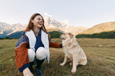 woman dog mountains nature smiling petting meadow outdoors: young woman kneeling in alpine meadow laughing as she pets her dog with scenic mountain range and clear sky behindの写真素材
