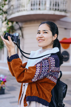 Candid shot of a woman photographing with a camera on a sunny street, wearing a patterned cardigan...