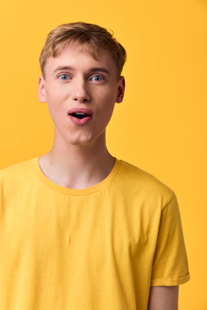 Surprised man in yellow shirt against a bold yellow backdrop, astonishment and open mouth expression...