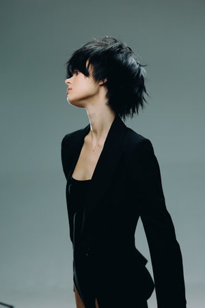 Profile of a young woman with short black hair wearing a black blazer against a solid grey...