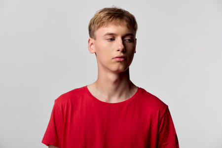 Young man in a red shirt stands against a neutral studio backdrop with calm expression, clean lighting, and a minimalist mood, suitable for fashion, lifestyle and product promotionの写真素材