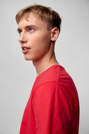 Young man in a red shirt, side profile against a plain backdrop, conveying focus and thoughtful...