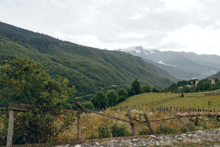 Scenic landscape featuring mountains and a green valley with rolling hills a rustic fence and trees...