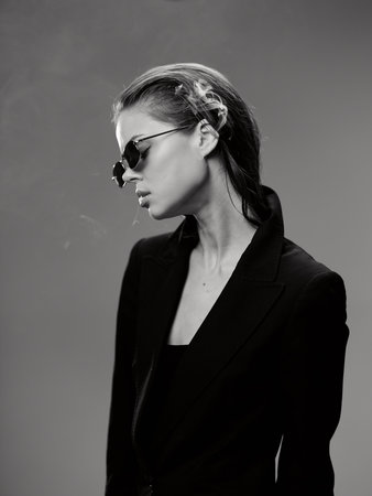 Black and white portrait of a stylish woman in sunglasses wearing a black blazer with a serious expression.の写真素材