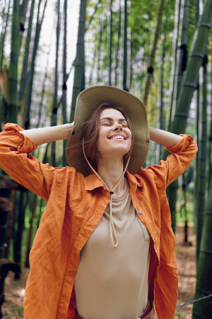 Woman with a relaxed smile wearing a wide brim hat in a dense bamboo forest, enjoying nature...