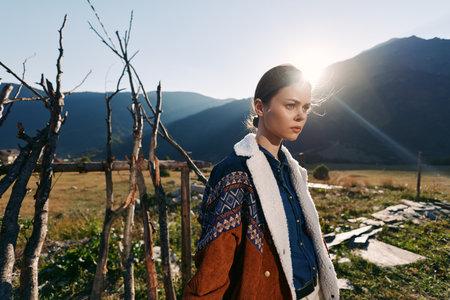 Woman portrait in countryside mountains with warm sunlight wearing a wool coat by a rustic fence,...