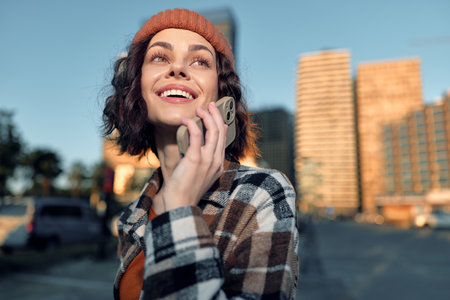 Woman on phone smiling in urban street at golden hour, candid lifestyle portrait capturing joyful conversation, authenticity and golden hour glow with mindful living and emotional storytelling.の写真素材