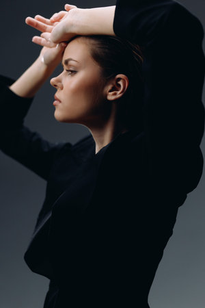 young woman posing with arms raised wearing black clothing against dark backgroundの写真素材