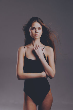 Young woman in black bodysuit posing confidently with flowing hair against neutral backgroundの写真素材
