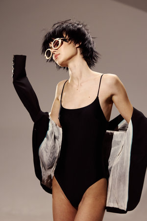 Stylish woman wearing black swimsuit and sunglasses posing with jacket, modern look, fashion,...
