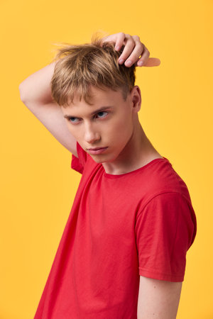 Male, young, scratching head, puzzled expression in a red shirt against bright yellow background,...