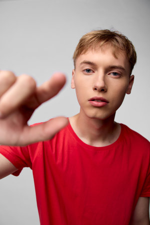 Young man in a red shirt extends his hand toward the camera in a close up studio shot, creating...