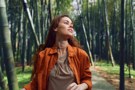 Woman forest bamboo portrait walking outdoor in orange jacket with gentle smile, looking up on a...