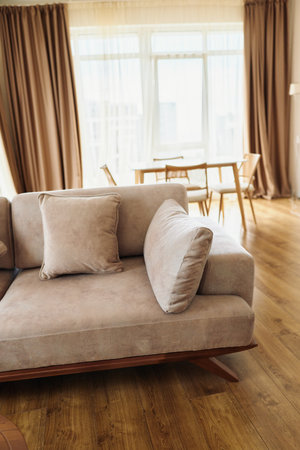 Sofa cushion livingroom hardwood curtains diningtable in a sunlit modern apartment interior, cozy neutral upholstery on wooden floor with minimalist dining area and soft natural light.の写真素材