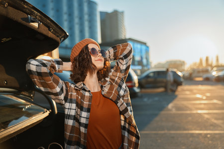 woman car parking sunlight urban sunglasses portrait of relaxed traveler leaning on open trunk during golden hour glow, a candid lifestyle scene of authenticity, mindful living and emotionalの写真素材