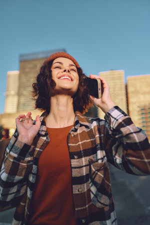 Woman on phone smiling in urban street during golden hour, candid lifestyle portrait with authenticity and emotional storytelling, beanie and flannel jacket, joyful mindful living vibe.の写真素材