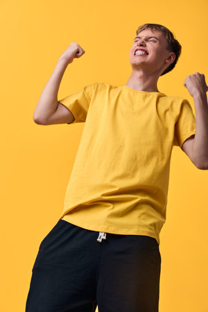 Boy in a bright yellow t shirt celebrates with clenched fists, energy and joy against a vivid yellow...