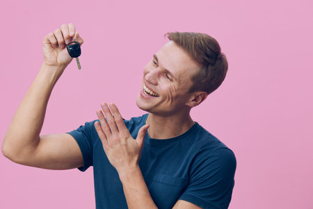 smiling man holding car key excited happy casual wear blue t-shirt pink background technology concept joyの写真素材
